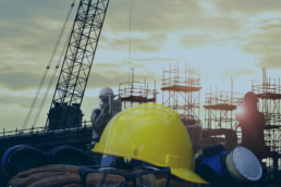 Cantiere industriale con casco di sicurezza giallo e impalcature al tramonto, simbolo della sicurezza aziendale e dell’importanza di un sistema RTLS per evacuazioni aziendali.